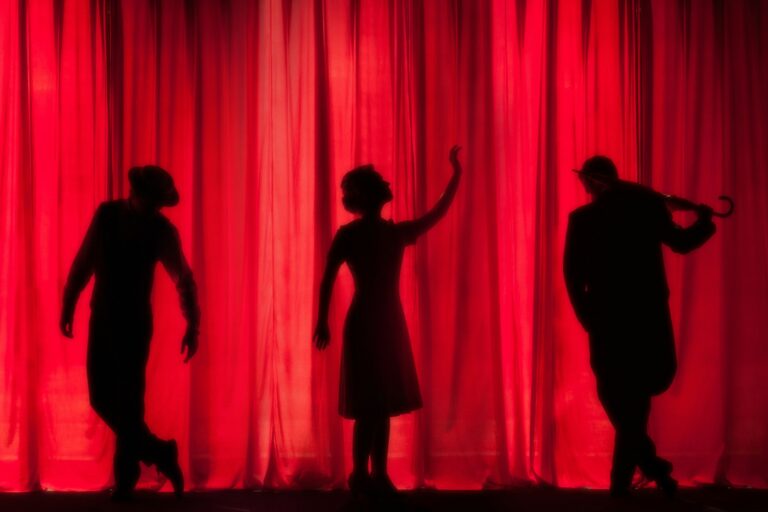 Silhouetten von drei Darsteller:innen auf einer Amateurtheaterbühne