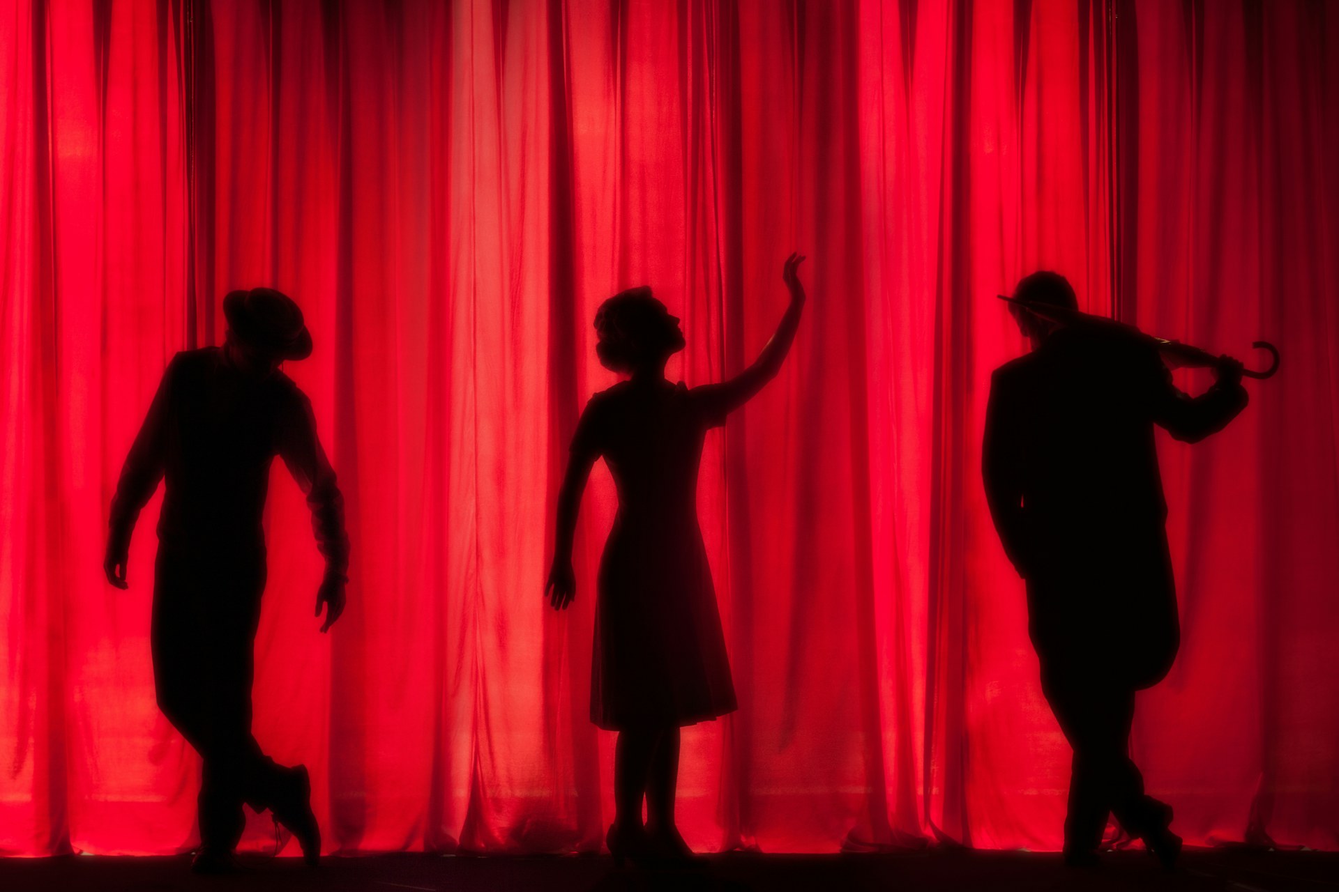 Silhouetten von drei Darsteller:innen auf einer Amateurtheaterbühne